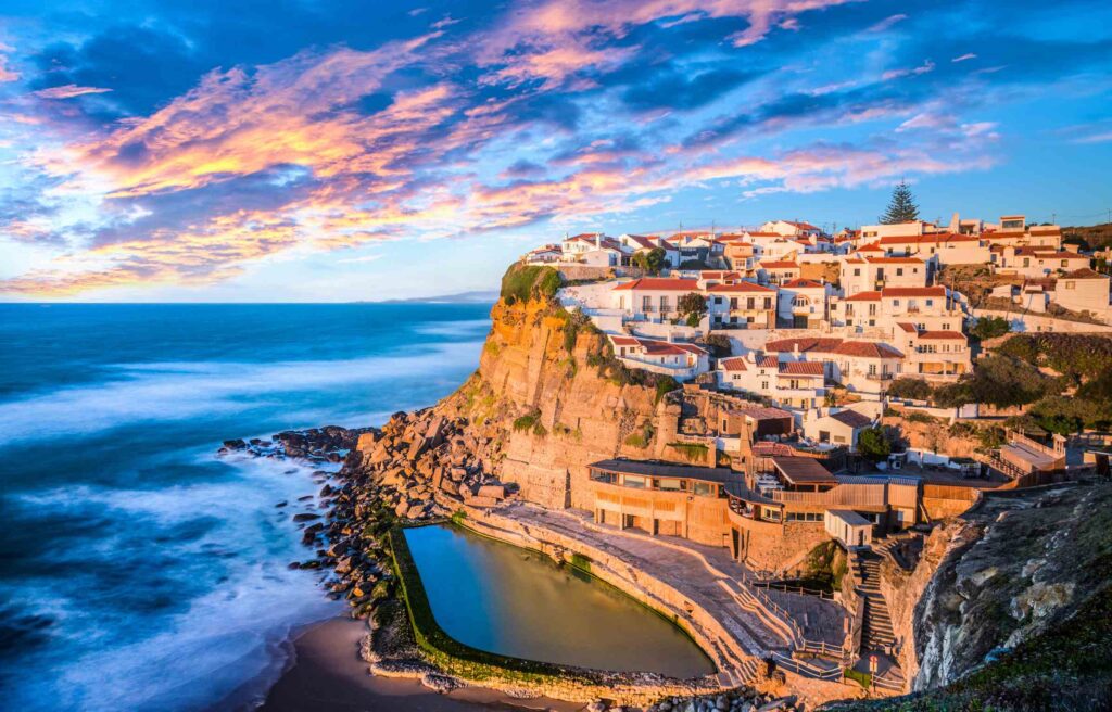 Cliffside village in Portugal with white houses, terracotta roofs, and ocean views at sunset.