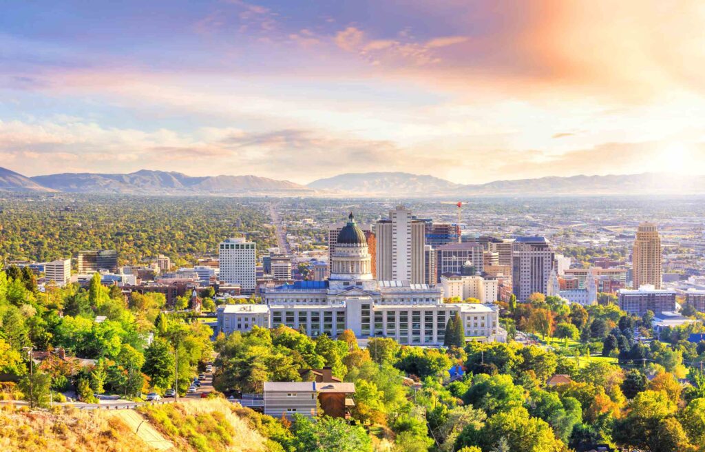 Salt Lake City skyline with the Utah State Capitol in the foreground and mountains in the background at sunset.