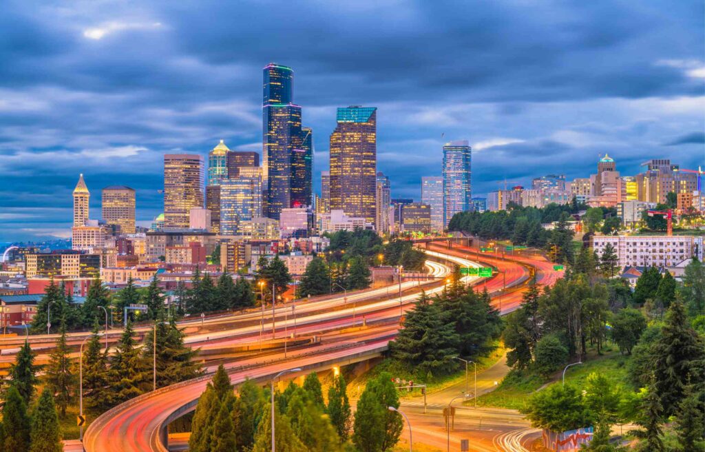 Seattle skyline at dusk with illuminated highways and downtown skyscrapers.