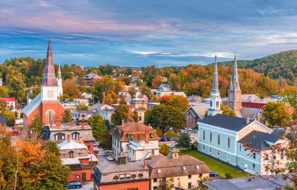 Scenic view of South Burlington, Vermont with colorful autumn trees, historic churches, and small-town architecture against rolling hills.