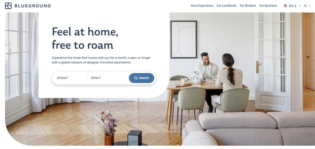The Blueground homepage features a digital nomad couple conversing at a dining table in a bright, modern apartment.