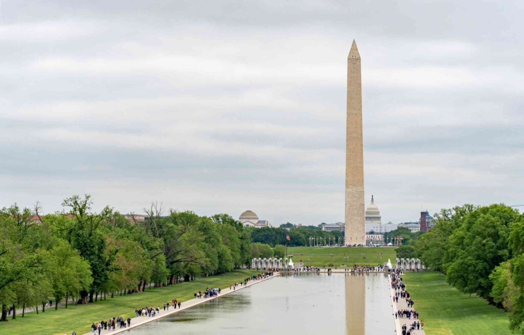 The Washington Monument with the Reflecting Pool and U.S. Capitol in the background on a cloudy day.