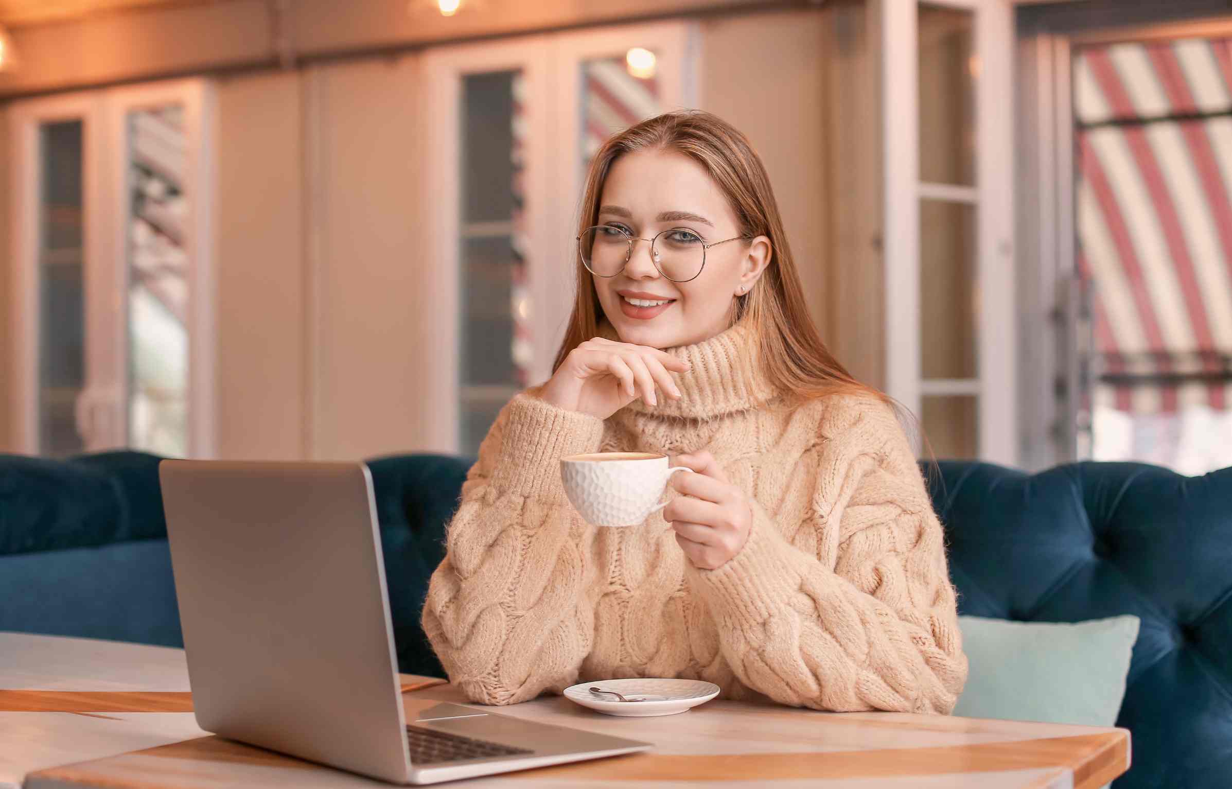A smiling woman in a cozy cafe, enjoying coffee while working on her laptop.