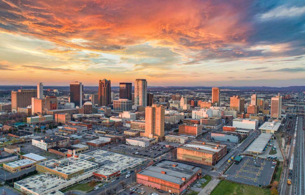 Aerial view of downtown Birmingham, Alabama, at sunset with city buildings and colorful skies.