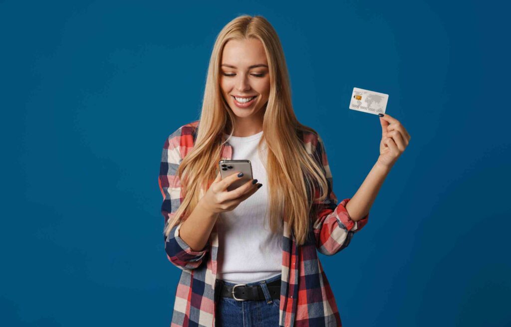 Smiling woman holding a credit card and smartphone, representing ways to earn atmos rewards points through everyday spending.