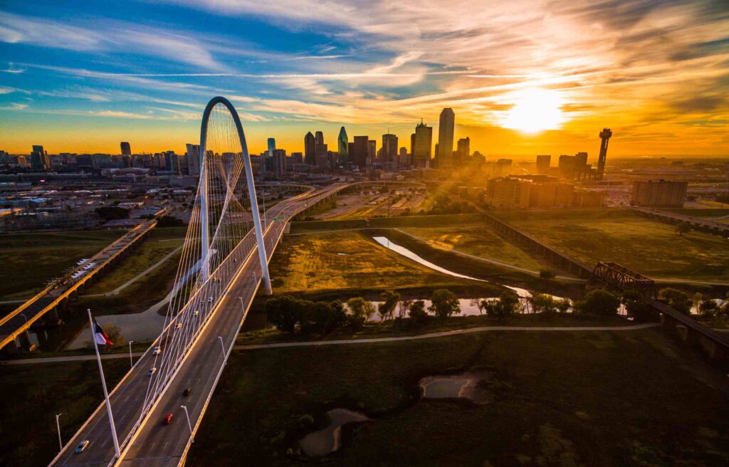 Aerial view of Dallas–Fort Worth, Texas, skyline at sunset with the Margaret Hunt Hill Bridge in the foreground.
