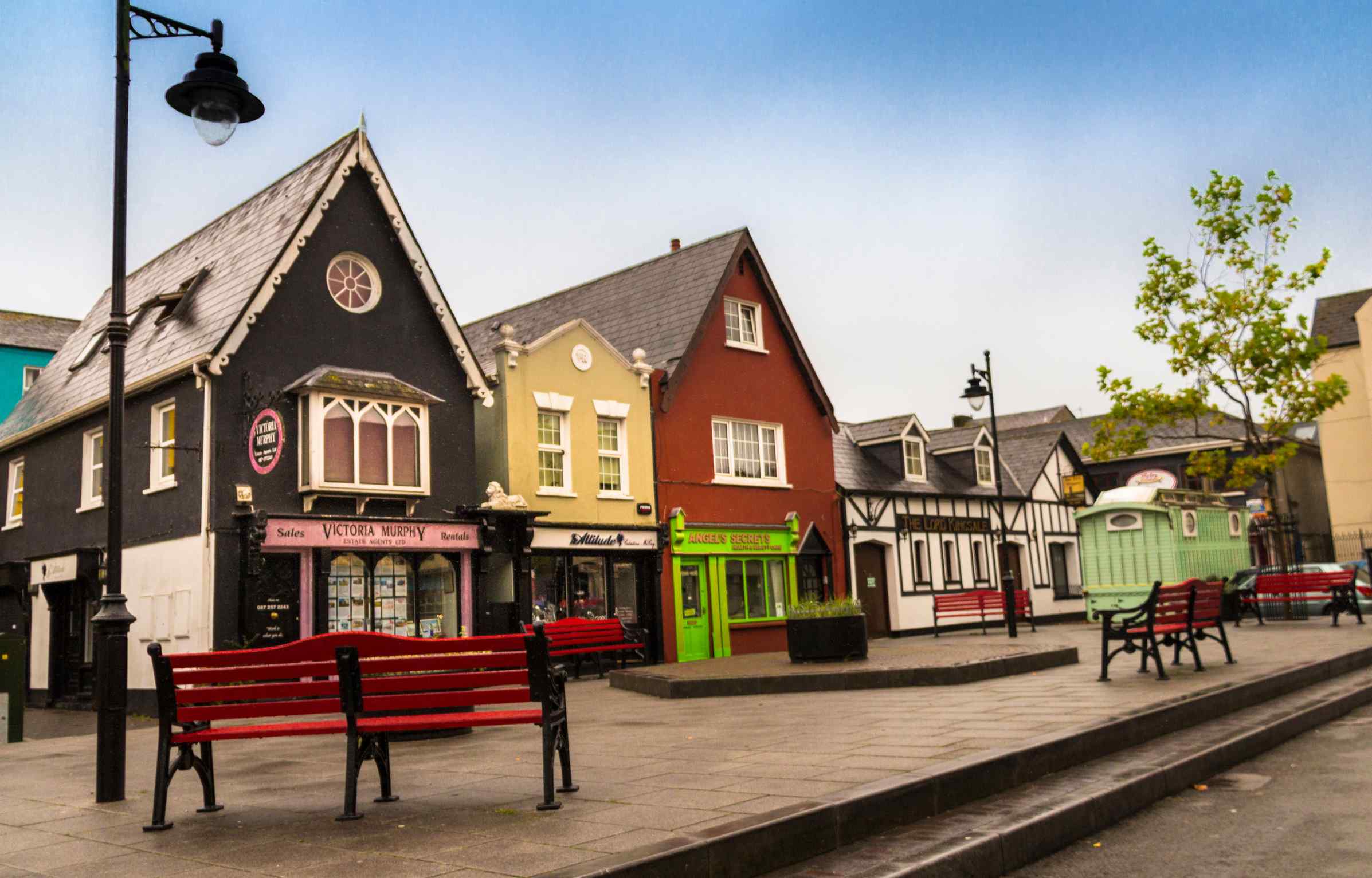 Colorful traditional houses and shops with red benches in an Irish town square.