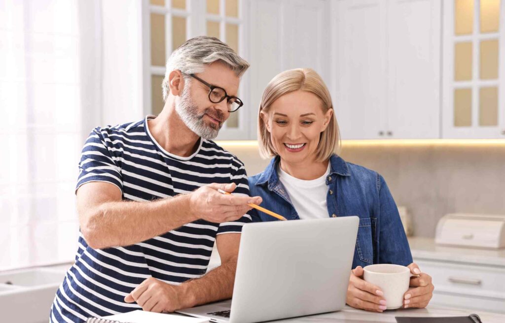 Smiling couple reviewing retirement plans on a laptop at home.