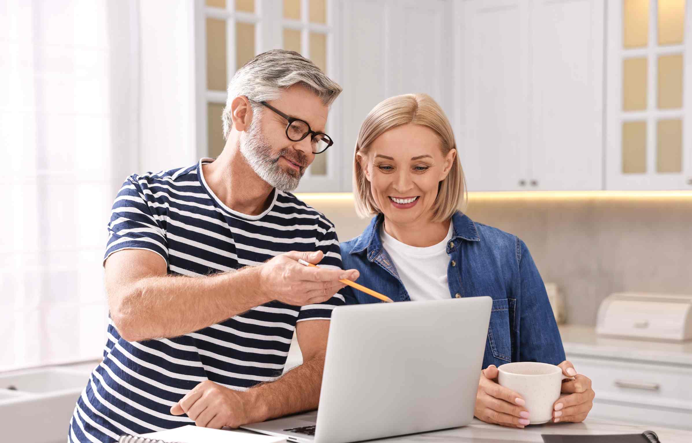 Smiling couple reviewing retirement plans on a laptop at home.