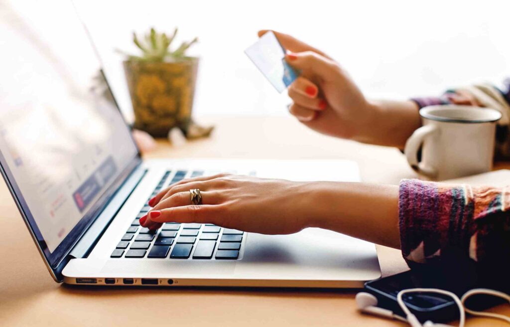 A woman uses her laptop while holding a credit card, checking details of the american express platinum credit card annual fee online.