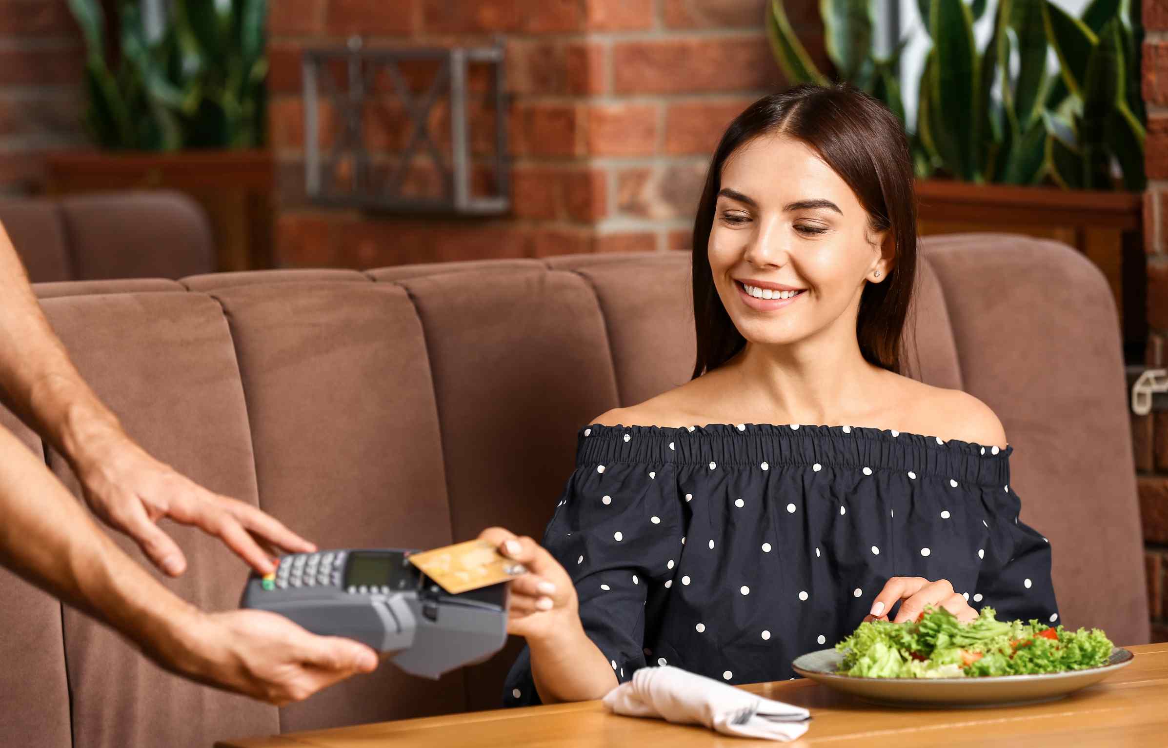 A woman is paying the bill at a restaurant using the highest cashback credit card while smiling at the server.