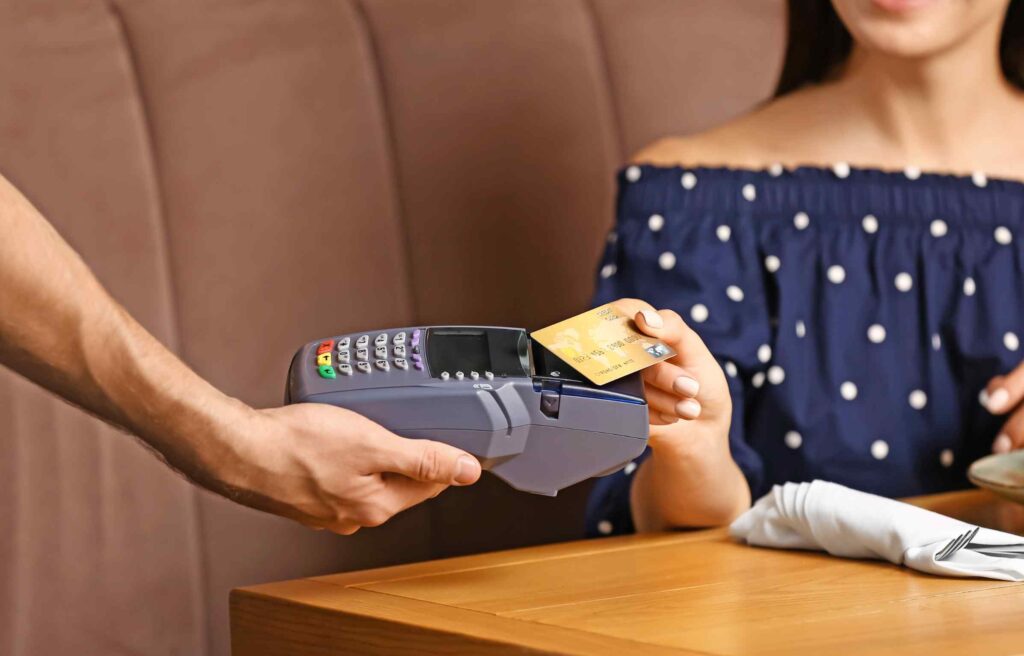 Woman paying a restaurant bill with the highest cashback credit card using a card machine at the table.