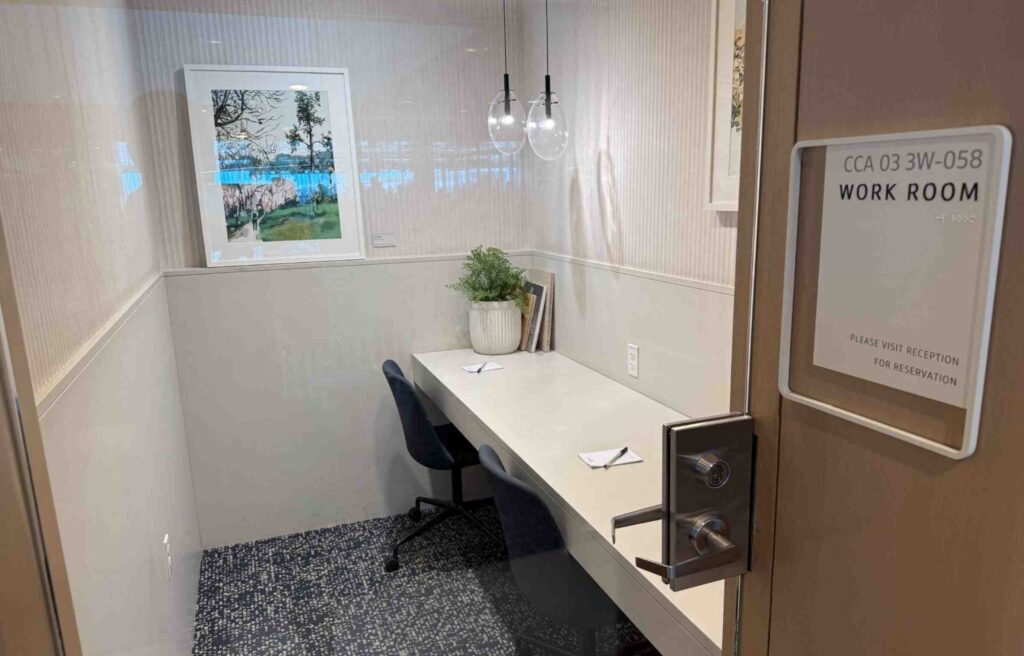 Small private workroom in the Capital One Lounge with two chairs, a desk, pendant lights, and framed artwork.