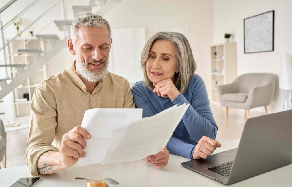 A happy middle-aged couple reviews retirement healthcare planning documents together at home.