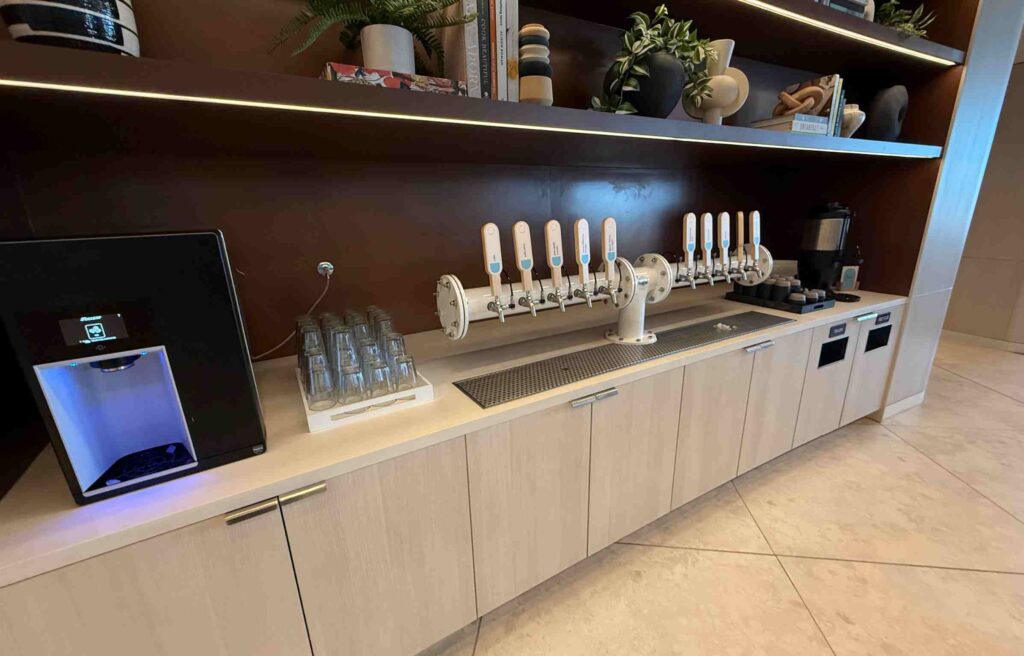 Counter with multiple beverage taps, glasses, and modern water dispensers for guest use.