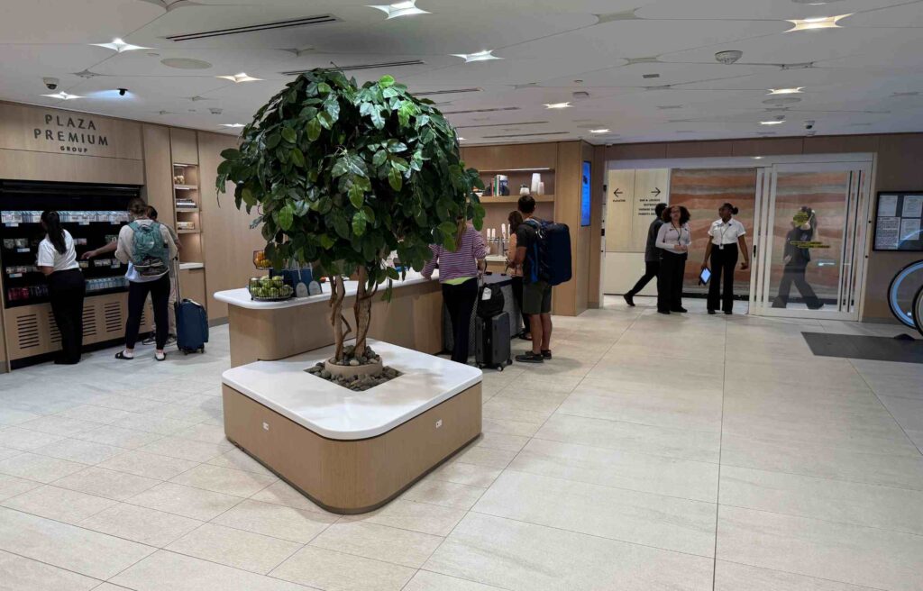 Travelers at the Capital One Lounge entrance with a refreshment counter and indoor tree.