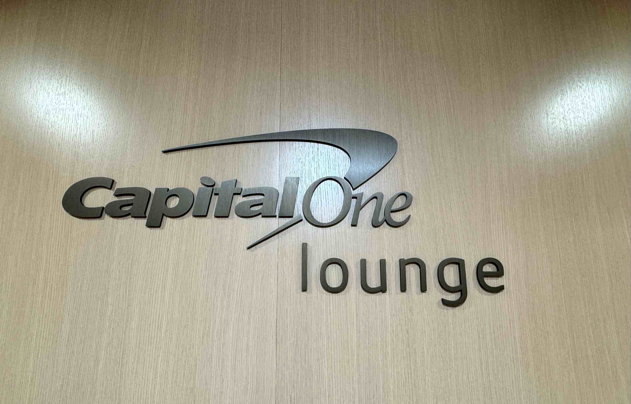 Close-up view of the Capital One Lounge logo displayed on a light wood wall at Denver International Airport.