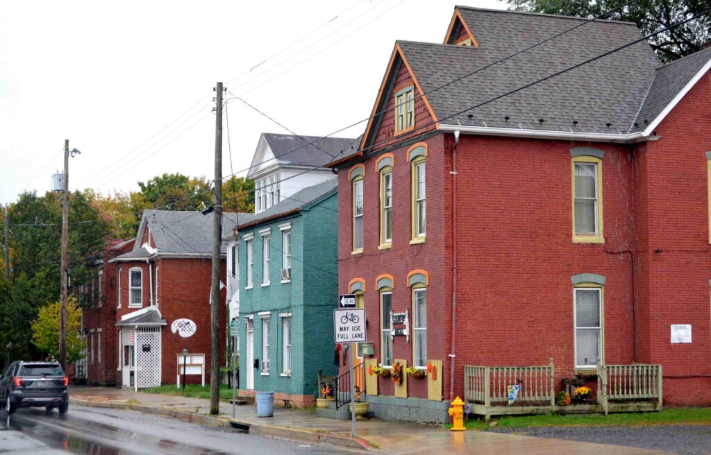 Colorful brick houses along a quiet street in downtown Cumberland, Maryland, on a rainy day with autumn trees in the background.