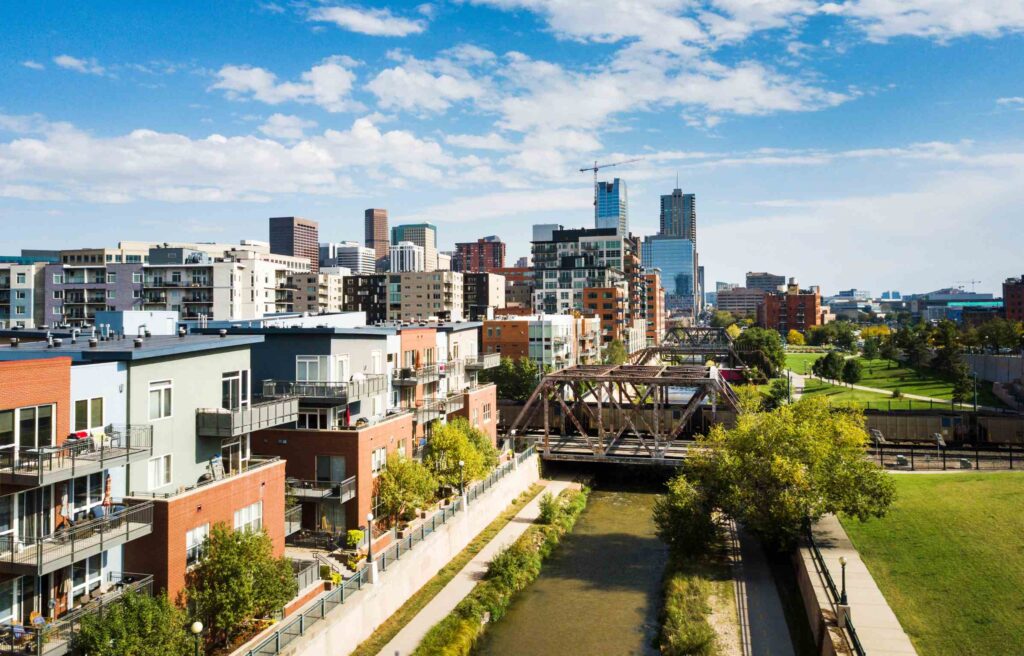 Denver, Colorado, city skyline with modern buildings and residential area along the river under a clear blue sky.