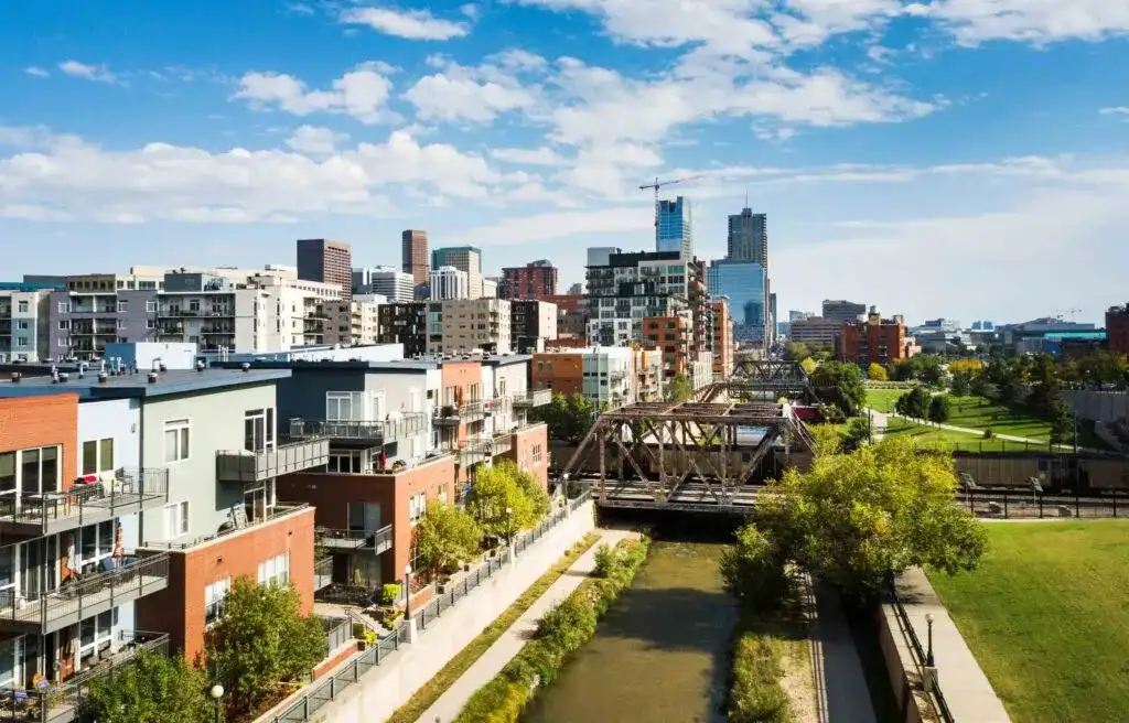 Denver, Colorado, city skyline with modern buildings and residential area along the river under a clear blue sky.

