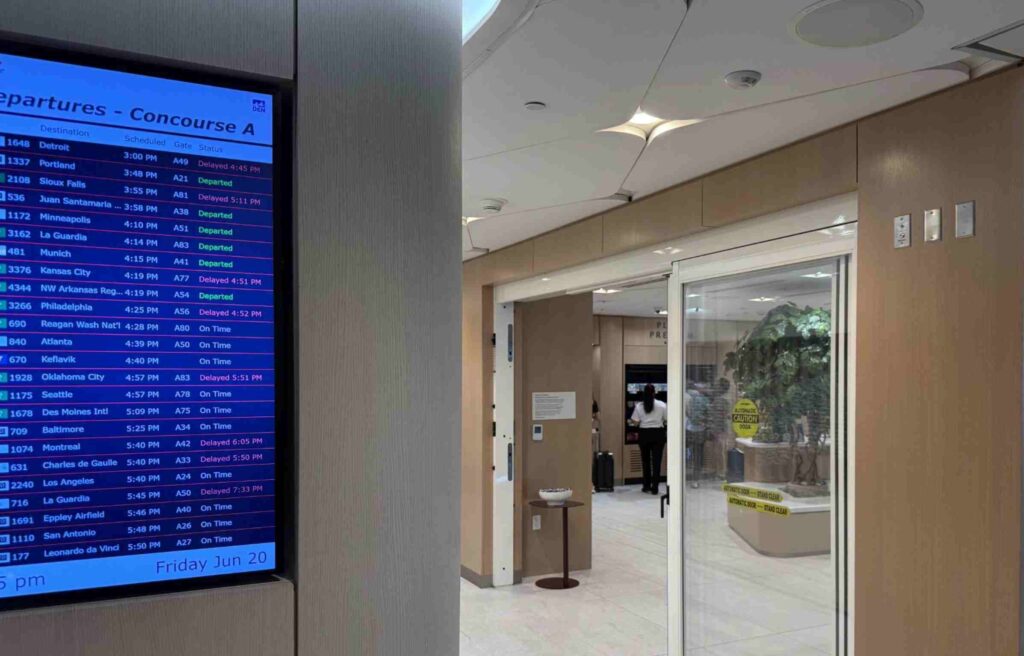 Flight departure screen showing Concourse A schedules beside the Capital One Lounge entrance.