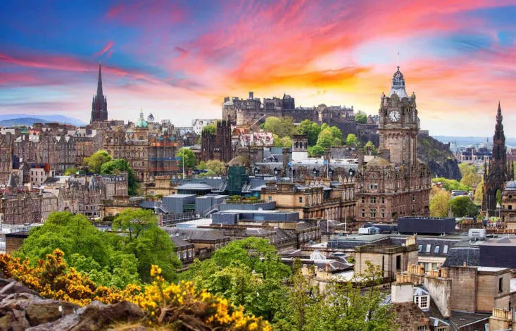 Panoramic view of Edinburgh, Scotland at sunset with the castle and city rooftops, capturing the charm of moving to scotland from the usa.