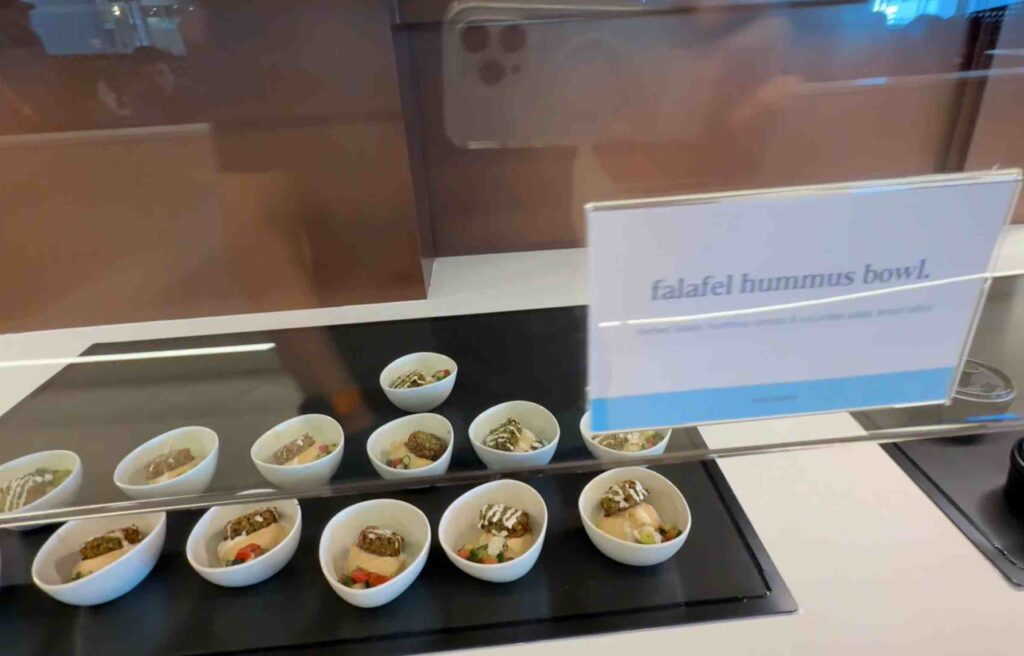 Small white bowls filled with falafel, hummus, and vegetables on a buffet counter.