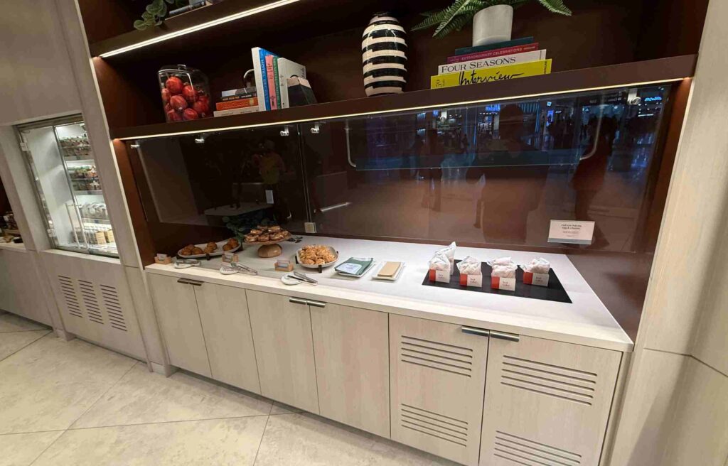 Assorted pastries, wraps, and sandwiches neatly arranged on a white countertop under warm lighting.