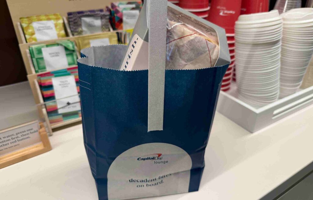 Capital One Lounge blue takeaway bag filled with snacks and drinks near tea selection.