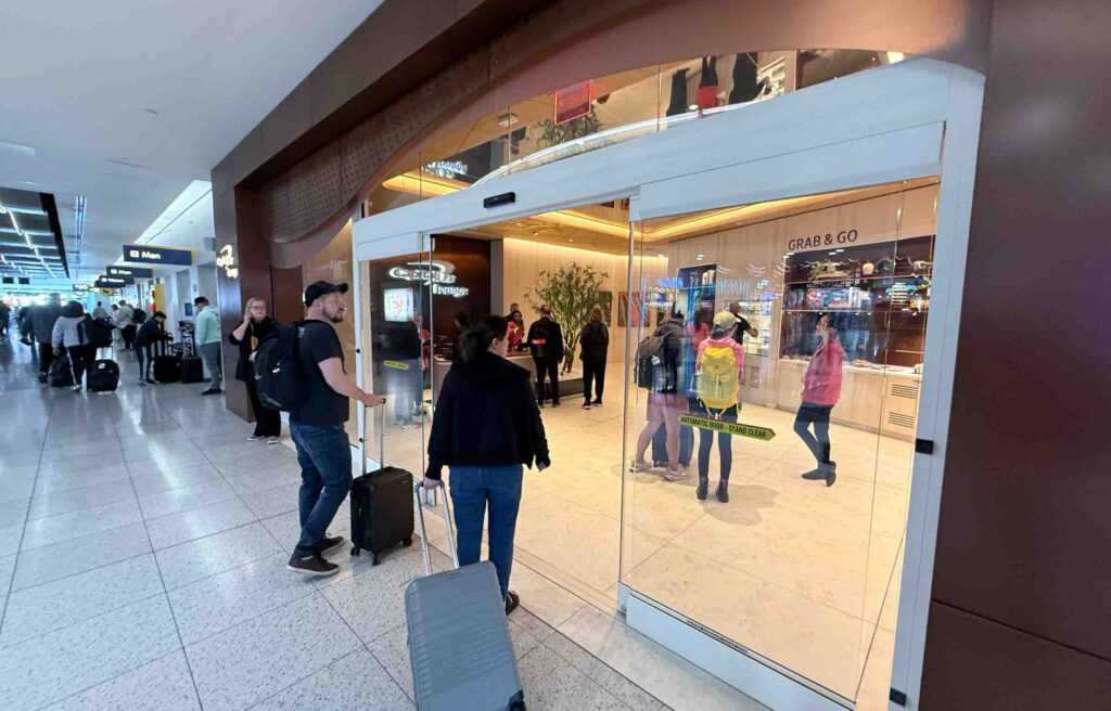 Travelers with luggage walking through glass doors into the Capital One Lounge.
