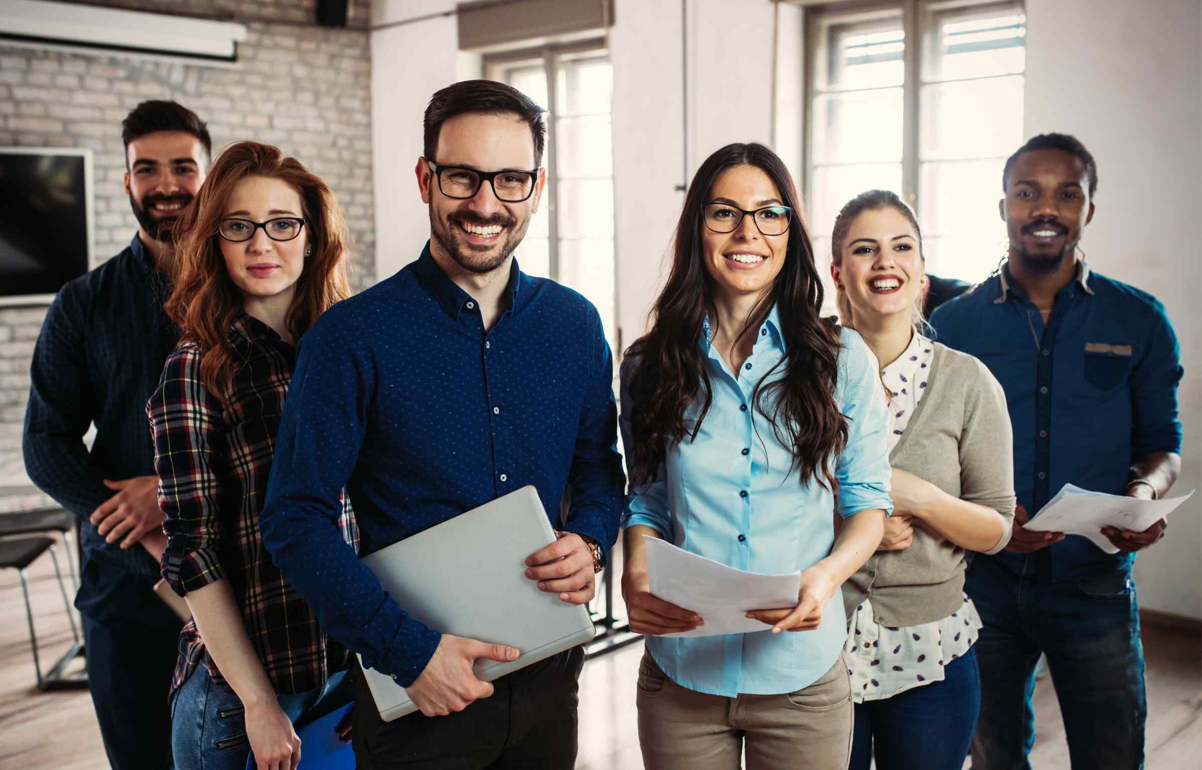 A group of happy employees standing together in an office, smiling at the camera.