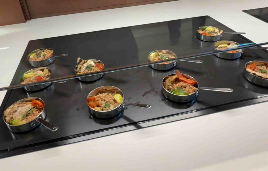 Mini metal pans filled with chicken, farro, and vegetables arranged on a counter.