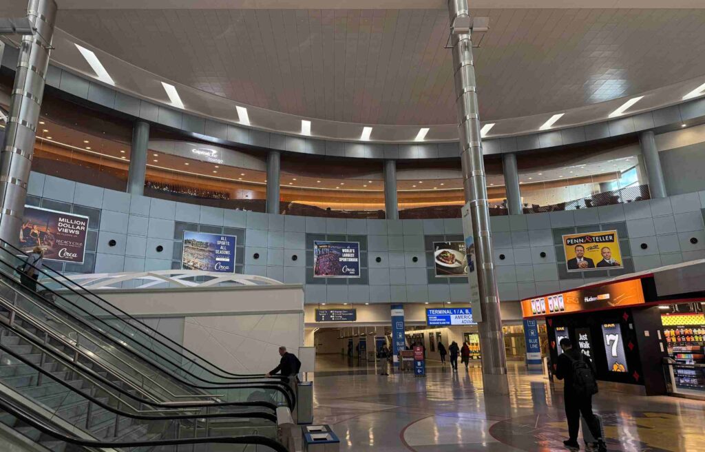 Airport interior showing escalators, shops, and the Capital One Lounge visible on the upper floor.