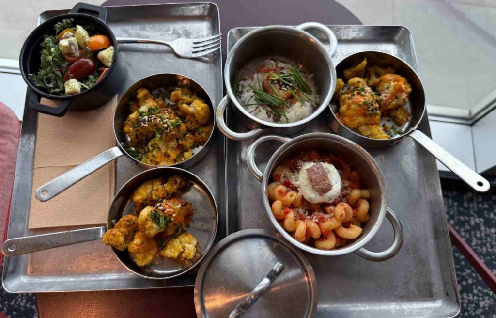 A tray with assorted dishes from the Capital One Lounge, including pasta pomodoro, curried cauliflower, and toy box caprese salad.