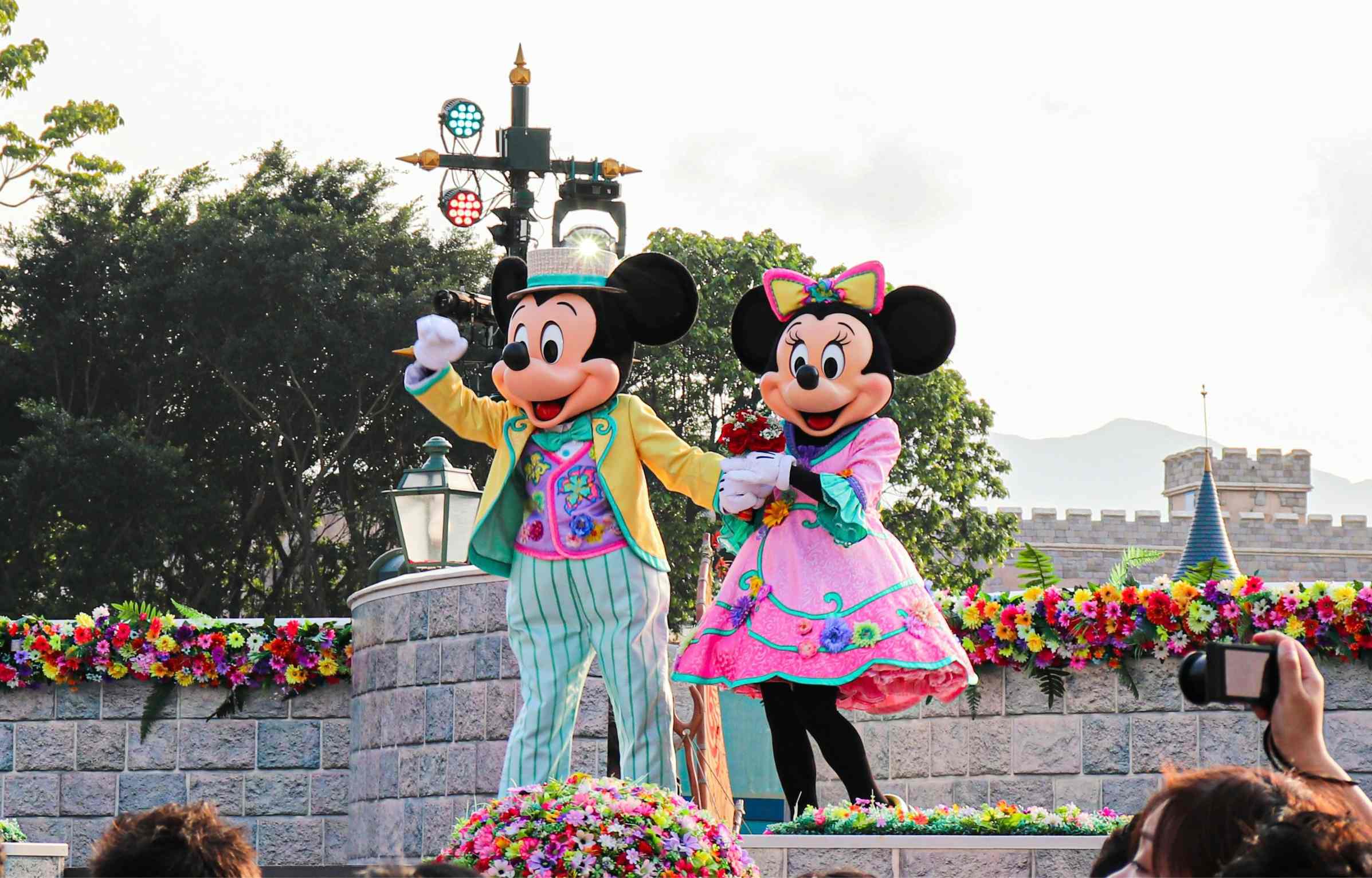 Feature image Mickey and Minnie in colorful outfits waving to a crowd during a Disney parade with bright flowers.