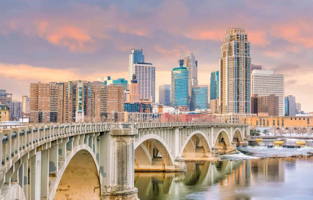 Skyline of Minneapolis, Minnesota, with a bridge over the Mississippi River at sunset, and a list of the top cities for female physicians to practice.
