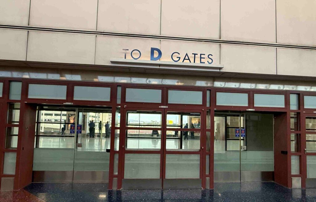 Entrance area leading to D Gates with glass doors and reflections on the polished floor near the capital one lounge at las vegas airport.