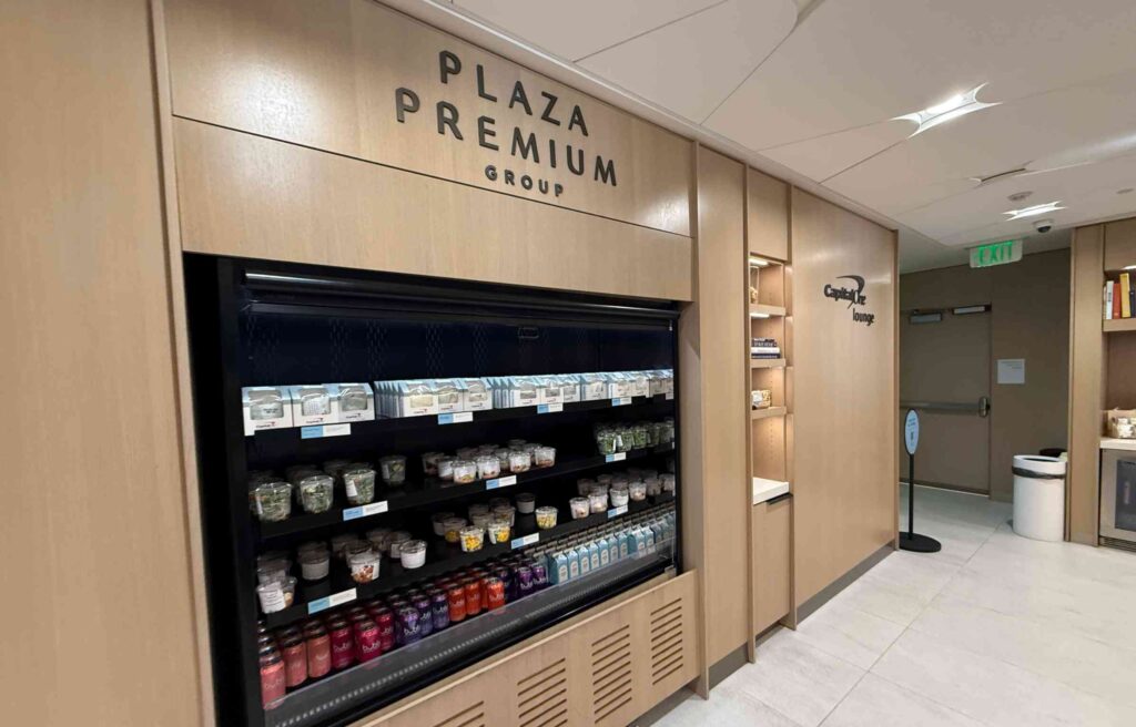 Plaza Premium Group refreshment area with neatly arranged salads, drinks, and snacks near the Capital One Lounge entrance at Denver Airport.