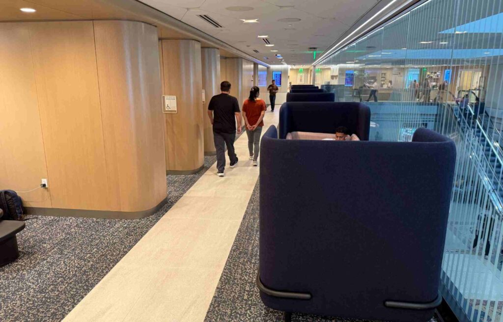 Hallway in the Capital One Lounge with private seating pods and travelers walking past glass walls overlooking the concourse.