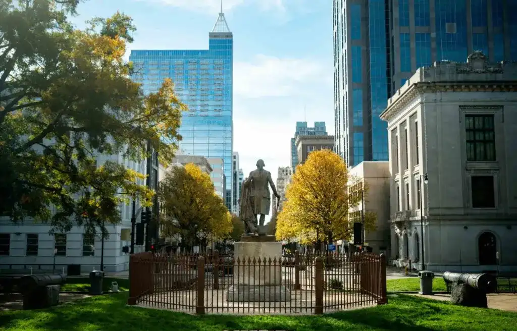 Raleigh, North Carolina, downtown view with historic statue, modern buildings, and trees in autumn colors.

