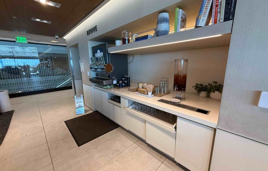 Revive section inside the Capital One Lounge featuring drink taps, iced tea dispenser, glassware, and neatly arranged décor items.