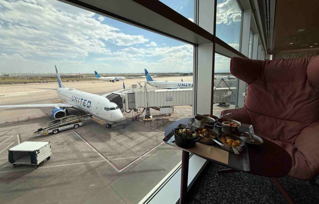 A cozy lounge chair by the window overlooking United Airlines planes with a meal tray set beside it.