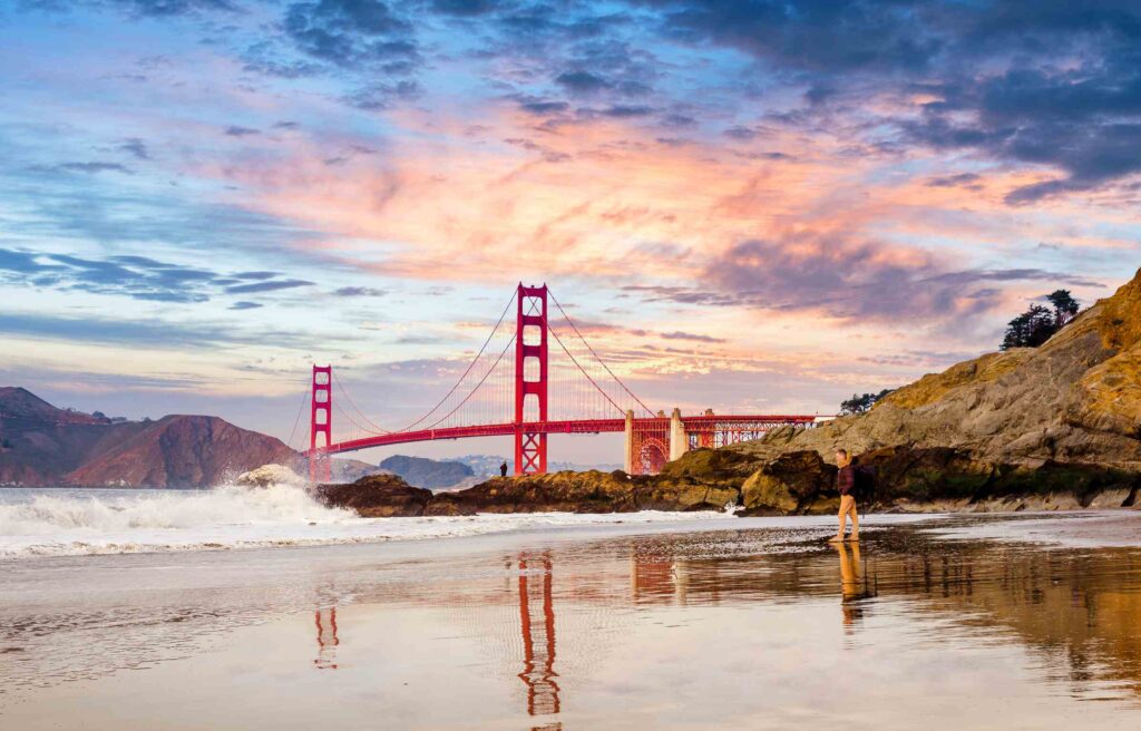 San Francisco, California, Golden Gate Bridge at sunset with waves crashing on the beach.