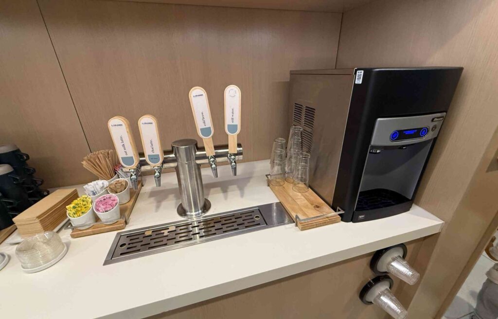 Self-serve drink station with taps for cold brew, still water, and oat latte at the Capital One Lounge.
