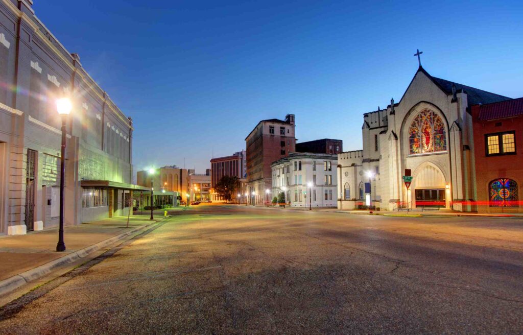 Evening view of downtown Texarkana, Texas, showing historic buildings and a church with stained glass windows illuminated under a clear sky.