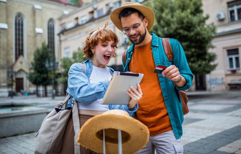 A cheerful couple holding a tablet and a credit card while planning a vacation, reflecting excitement and curiosity about, and reading, is disney premier visa card worth it?