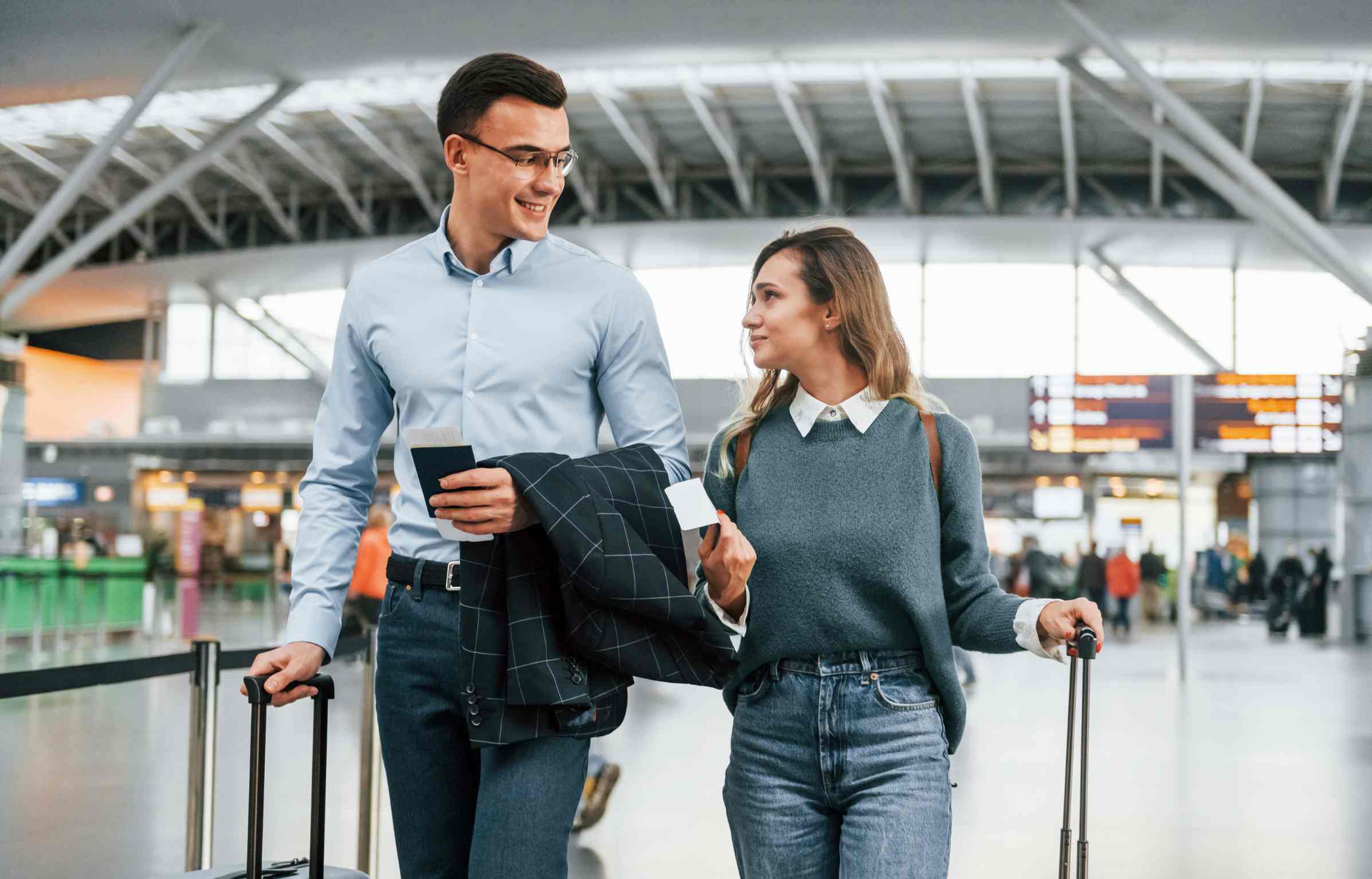 A smiling couple walking through the airport terminal with luggage and boarding passes, ready for their flight.