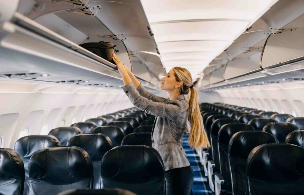 Woman storing her carry-on bag in the airplane’s overhead compartment before takeoff.