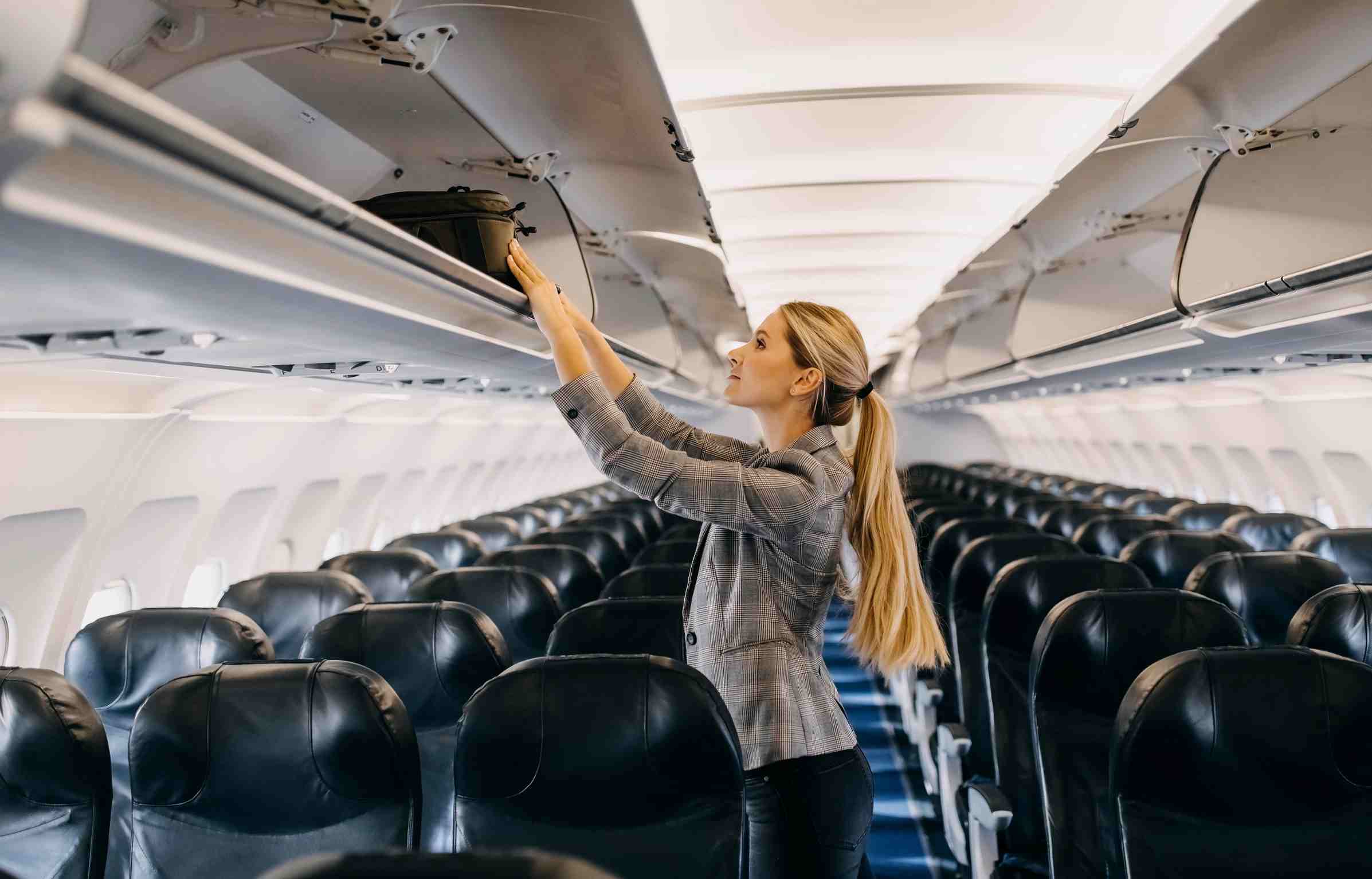 Feature image Woman storing her carry-on bag in the airplane’s overhead compartment before takeoff.
