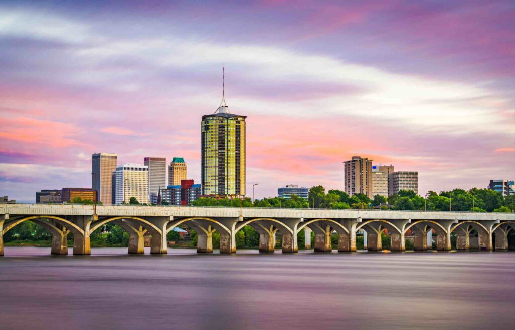 The skyline of downtown Tulsa, Oklahoma, at sunset, with the Arkansas River and bridge in view, highlights one of the top cities with remote work incentives.